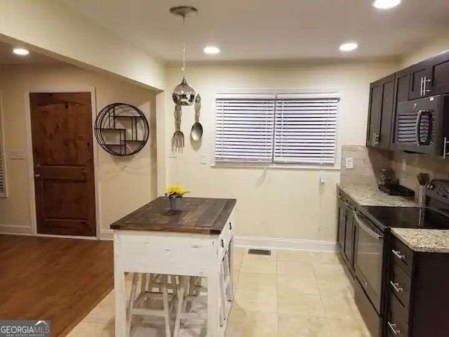 kitchen with stainless steel electric range, hanging light fixtures, light stone countertops, light hardwood / wood-style floors, and decorative backsplash