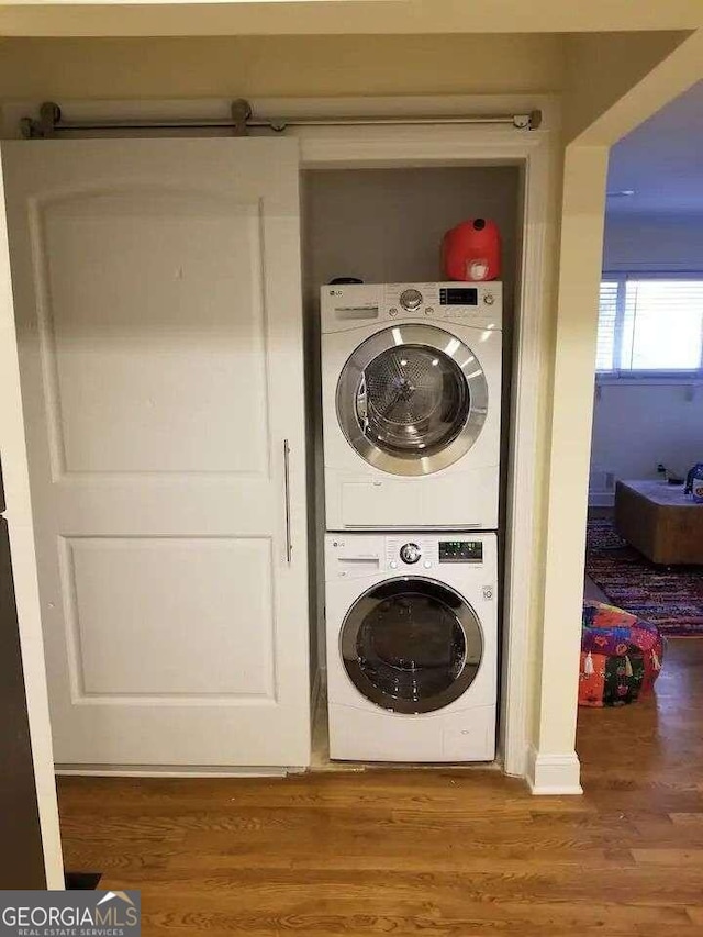 laundry area with hardwood / wood-style floors and stacked washer and clothes dryer