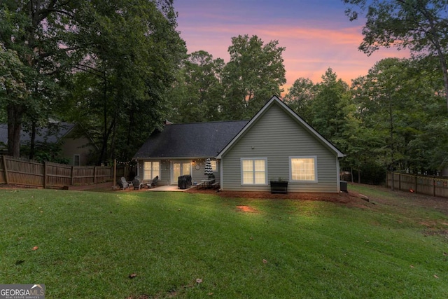 back house at dusk featuring a lawn