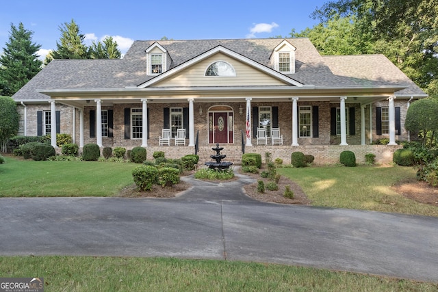 view of front of house featuring brick siding, roof with shingles, a porch, and a front yard