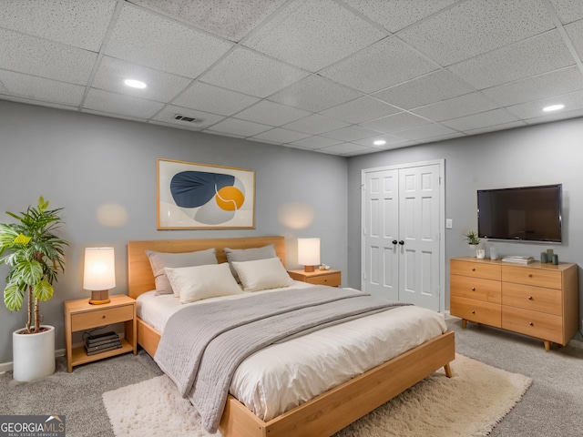 carpeted bedroom with a paneled ceiling and a closet