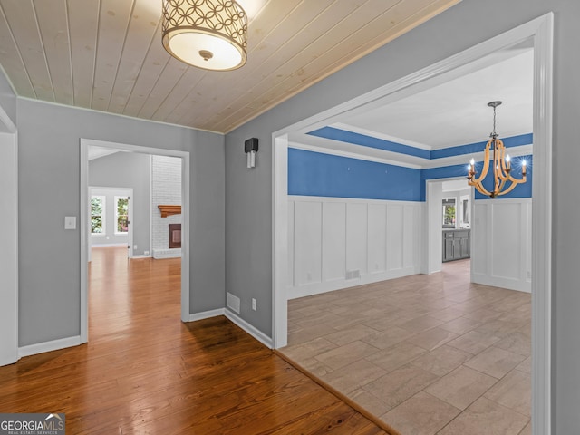 interior space featuring wooden ceiling, a brick fireplace, light hardwood / wood-style flooring, crown molding, and a chandelier