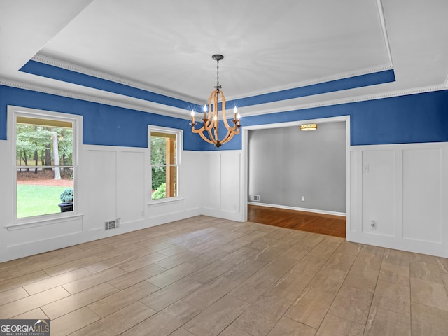 unfurnished dining area with a tray ceiling, a chandelier, and light wood-type flooring