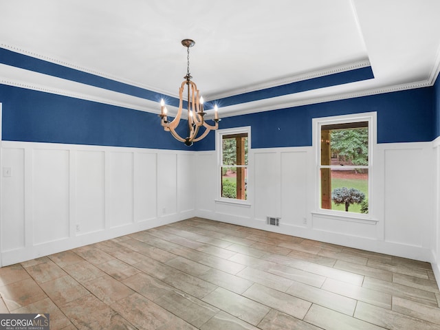 unfurnished dining area with a raised ceiling, crown molding, light wood-type flooring, and an inviting chandelier