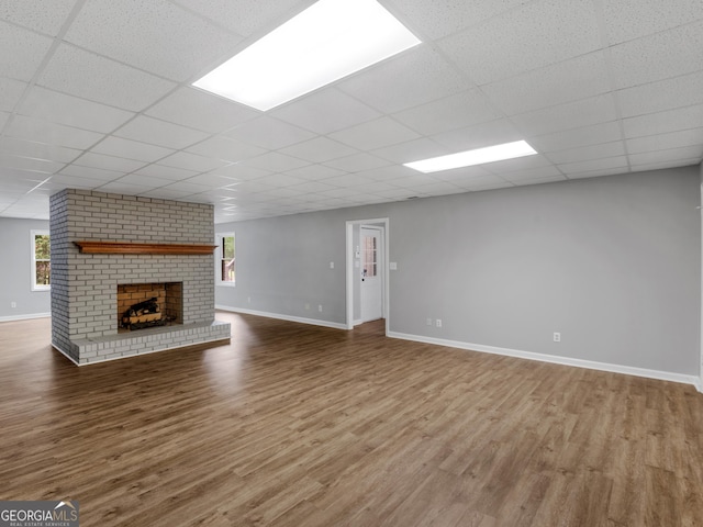 unfurnished living room featuring a paneled ceiling, hardwood / wood-style floors, plenty of natural light, and a brick fireplace