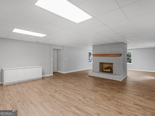 unfurnished living room featuring light wood-type flooring, a brick fireplace, and a drop ceiling