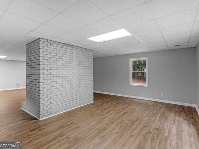 interior space featuring a paneled ceiling, brick wall, and light wood-type flooring