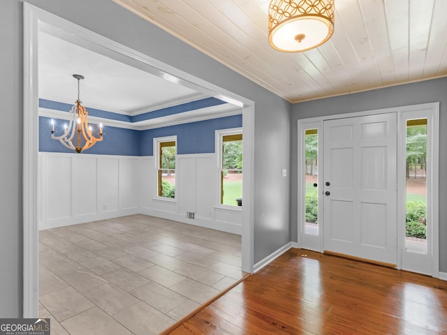 foyer entrance featuring ornamental molding, an inviting chandelier, wooden ceiling, and a healthy amount of sunlight