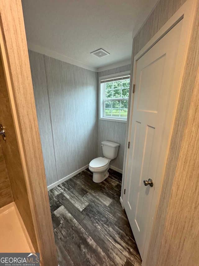 bathroom with wood-type flooring, toilet, wooden walls, and a textured ceiling