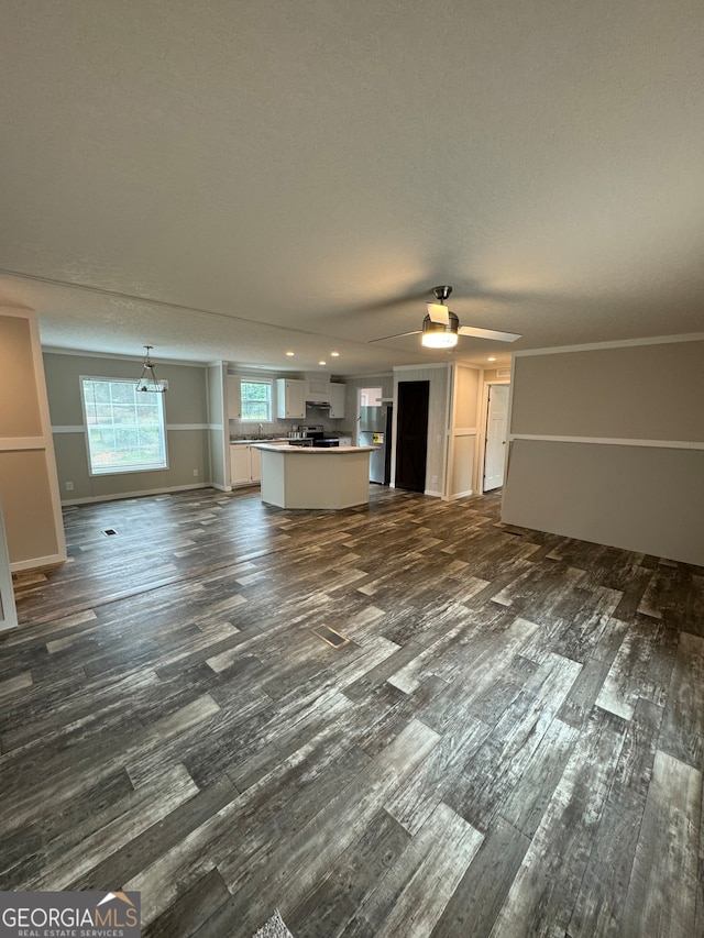 unfurnished living room featuring ceiling fan, dark hardwood / wood-style flooring, a textured ceiling, and ornamental molding