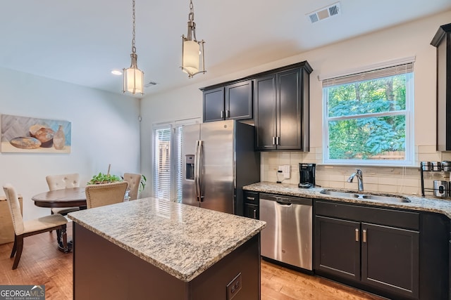 kitchen with light wood-type flooring, decorative light fixtures, a kitchen island, sink, and appliances with stainless steel finishes