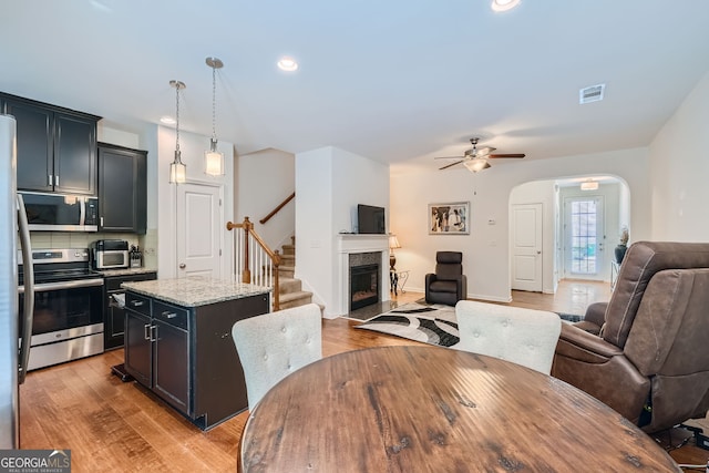 kitchen with decorative light fixtures, a kitchen island, ceiling fan, appliances with stainless steel finishes, and light hardwood / wood-style floors