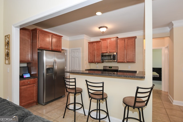 kitchen featuring stainless steel appliances, light tile patterned floors, ornamental molding, and a breakfast bar