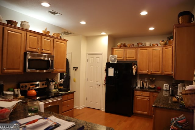 kitchen with appliances with stainless steel finishes, dark stone counters, and light hardwood / wood-style flooring