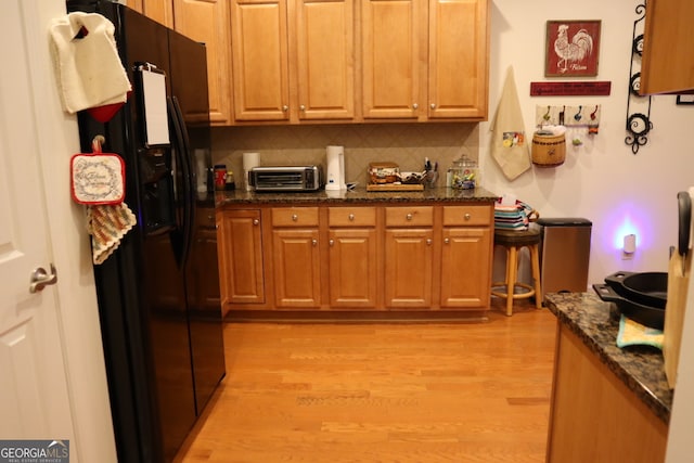 kitchen featuring light wood-type flooring, dark stone countertops, backsplash, and black fridge with ice dispenser