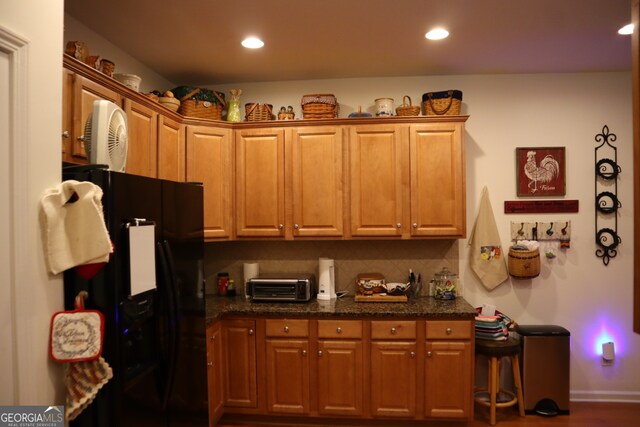 kitchen featuring dark hardwood / wood-style floors, dark stone counters, and black fridge