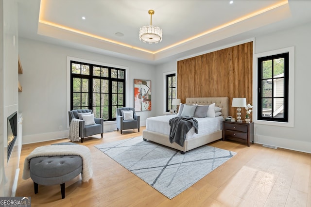 bedroom with a tray ceiling, multiple windows, and light hardwood / wood-style flooring