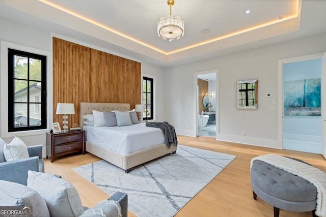 bedroom with a tray ceiling, ensuite bath, wood-type flooring, and multiple windows