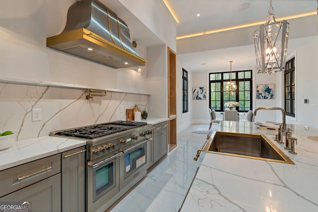 kitchen featuring light stone counters, a chandelier, gray cabinets, wall chimney exhaust hood, and range with two ovens