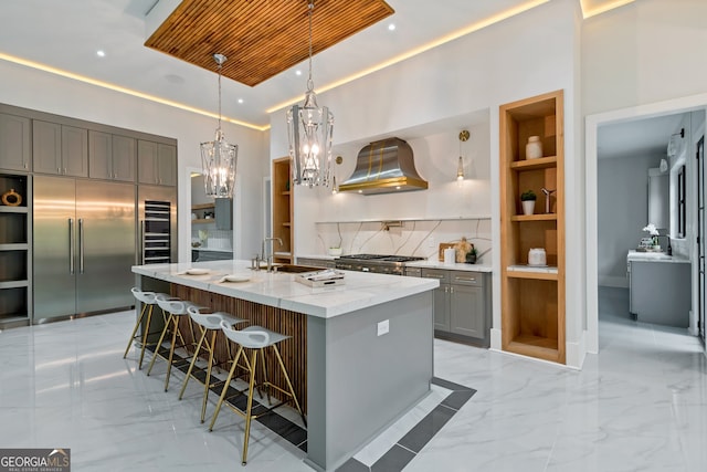 kitchen featuring decorative light fixtures, stainless steel appliances, sink, exhaust hood, and a center island with sink