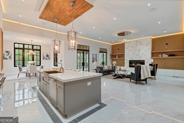 kitchen featuring decorative light fixtures, a center island with sink, a premium fireplace, an inviting chandelier, and stainless steel dishwasher