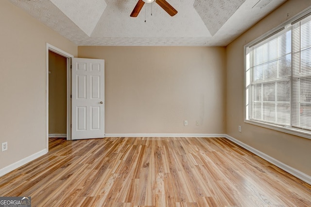 unfurnished room featuring ceiling fan, a raised ceiling, a textured ceiling, and light wood-type flooring