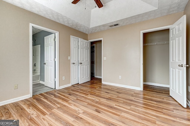 unfurnished bedroom featuring ensuite bath, a textured ceiling, light wood-type flooring, multiple closets, and ceiling fan