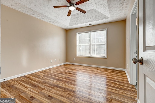 spare room with ceiling fan, a tray ceiling, a textured ceiling, and light wood-type flooring