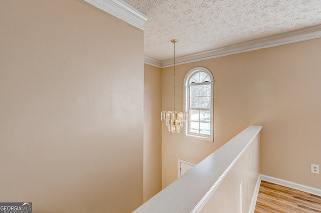 hallway with ornamental molding, a chandelier, a textured ceiling, and light hardwood / wood-style flooring