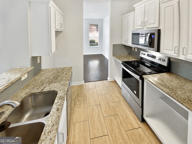 kitchen with light wood-type flooring, light stone counters, stainless steel appliances, and white cabinets