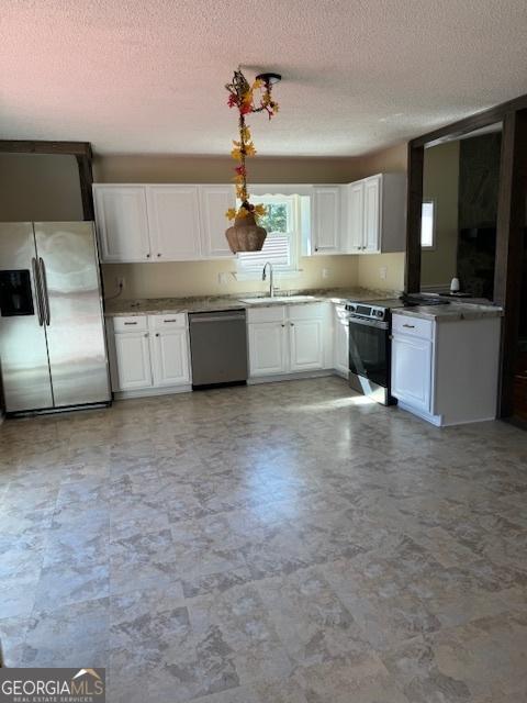 263 Hardin Rd SW, Plainville, GA 30733 - kitchen with a textured ceiling, white cabinets, a sink, hanging light fixtures, and stainless steel appliances