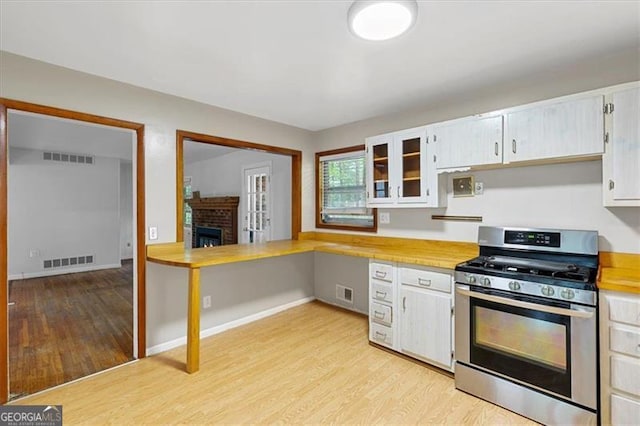 kitchen with stainless steel gas stove, light wood-type flooring, white cabinetry, and a fireplace