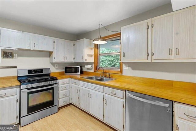 kitchen featuring hanging light fixtures, stainless steel appliances, sink, and light hardwood / wood-style floors