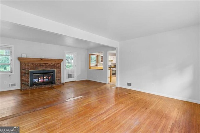 unfurnished living room with light hardwood / wood-style flooring and a brick fireplace