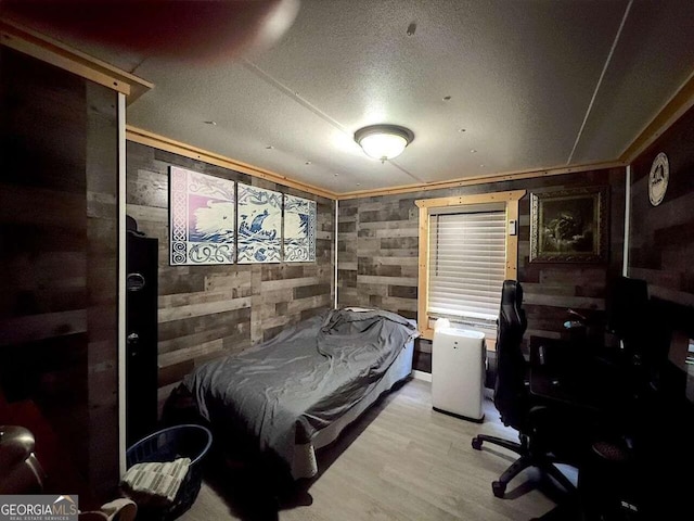 bedroom with a textured ceiling, light wood-type flooring, and wooden walls