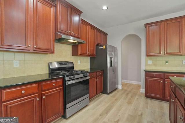 kitchen featuring light wood-type flooring, dark stone counters, stainless steel appliances, and decorative backsplash