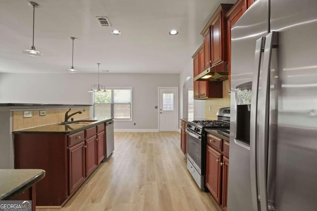 kitchen with pendant lighting, sink, decorative backsplash, appliances with stainless steel finishes, and light hardwood / wood-style floors