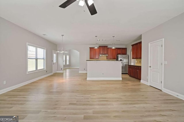 kitchen with stainless steel refrigerator with ice dispenser, an island with sink, hanging light fixtures, ceiling fan, and light wood-type flooring