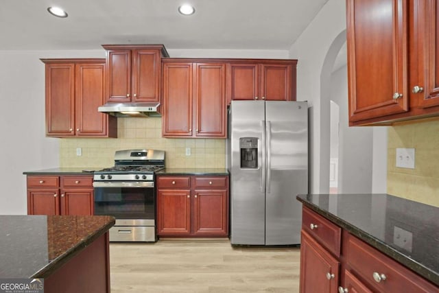 kitchen featuring backsplash, dark stone countertops, stainless steel appliances, and light hardwood / wood-style flooring