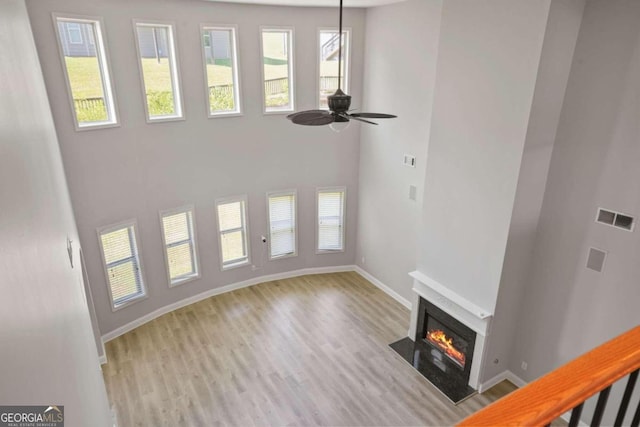 unfurnished living room featuring light hardwood / wood-style flooring, ceiling fan, a towering ceiling, and a healthy amount of sunlight