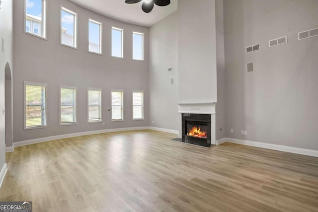 unfurnished living room featuring a towering ceiling, light hardwood / wood-style flooring, and ceiling fan