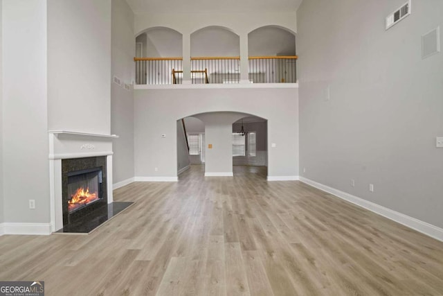 unfurnished living room featuring light hardwood / wood-style floors, a high end fireplace, and a towering ceiling