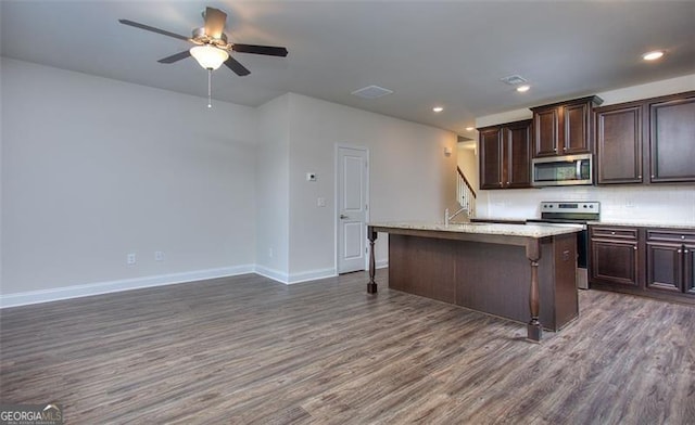 kitchen featuring dark wood-type flooring, a kitchen breakfast bar, a center island with sink, appliances with stainless steel finishes, and ceiling fan