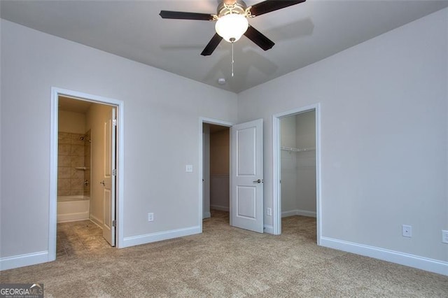 unfurnished bedroom featuring a spacious closet, connected bathroom, a closet, ceiling fan, and light carpet