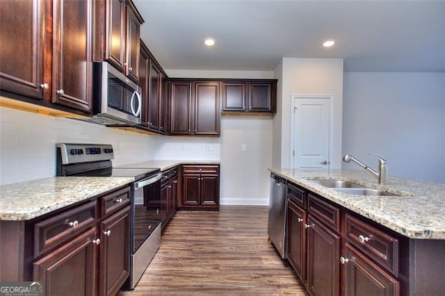 kitchen with sink, a kitchen island with sink, stainless steel appliances, light stone countertops, and dark hardwood / wood-style flooring