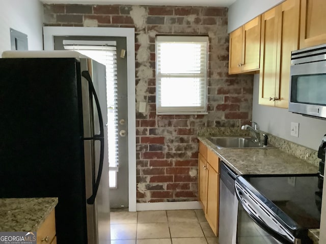 kitchen with brick wall, light stone countertops, light tile patterned floors, stainless steel appliances, and sink