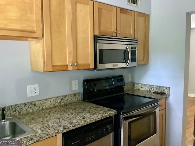 kitchen with appliances with stainless steel finishes, hardwood / wood-style flooring, light stone counters, and sink