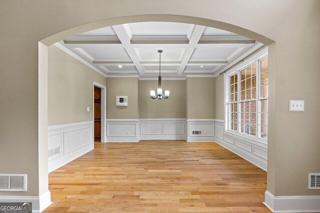 unfurnished dining area with coffered ceiling, crown molding, a chandelier, beam ceiling, and light hardwood / wood-style floors