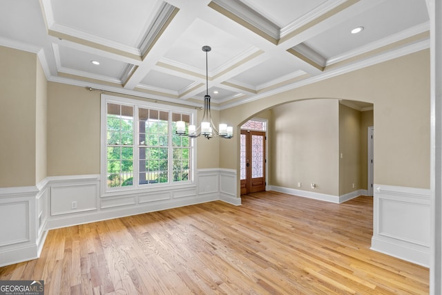 empty room featuring light wood-type flooring, coffered ceiling, a notable chandelier, and ornamental molding