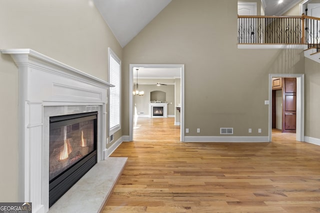 unfurnished living room featuring a high end fireplace, light wood-type flooring, and high vaulted ceiling